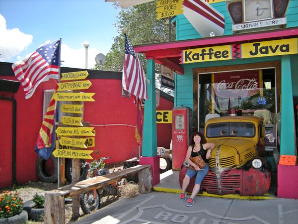 Lady sitting on old jalopy fender at store, signpost, colorful store front