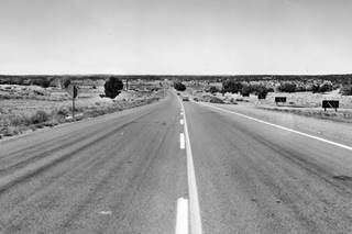 Route 66 in Houck, 1964 black and white photo, 2 lane US66 arid scenery, car heading west, trees and a pile placing machine