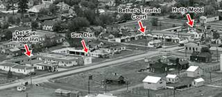 black and white 1930s aerial view of eastern Williams, Route 66 and motels along it. Homes, streets, railroad tracks and wagons. Forested hills.