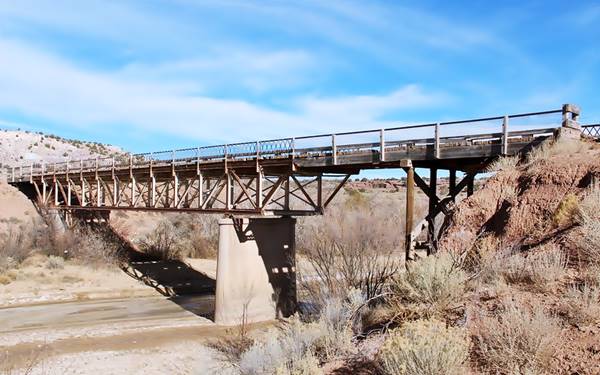 steel bridge with mid river concrete pier crosses a wide canyon with bushes and stream below