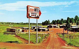 1950s color postcard, circle of cabins, dirt road leading to them, neon sign and field with trees