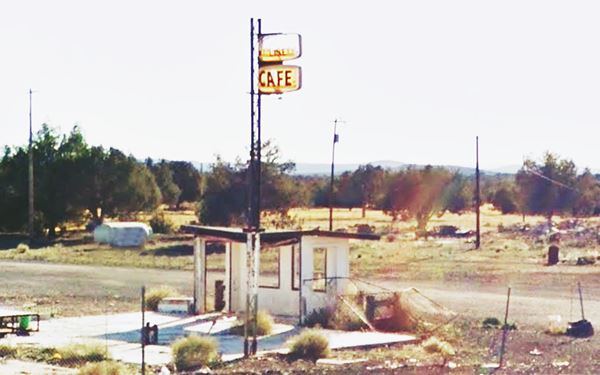 rubble, foundations, tottering walls and steel pole to the left and one to the right with two neon sign boxes, only yellow plastic remains, word CAFE written in red letters on lower box