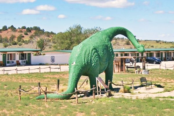 Zoomie fiberglass dinosaur statue Route 66 Arizona green apatosaurus statue with motel behind and Route 66 shield painted on wall