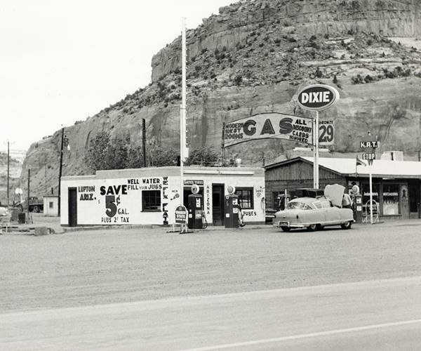 Indian Trails Dixie gas station by Ed Ruscha 1962 black and white photo Dixie El Paso block shaped gas station and pumps left, signage with gas price and long timber faced, gable roofed trading post and cars seen from old US66, in 1962