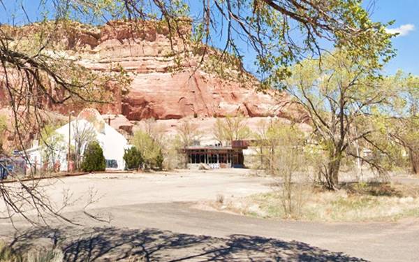 dome with a crest, vacant, drive and parking area, vacant decrepit gas station to the right, cliffs behind, trees around it, seen from old US66