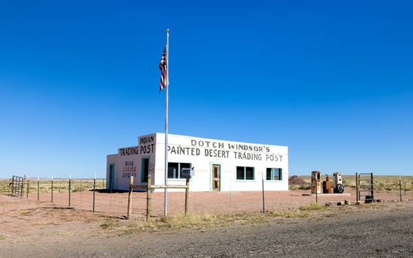 white building with 2 vintage gas pumps. With signs indicating it is Dotch Trading Post, American flag on mast to the left