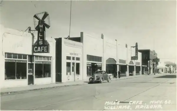 black and white postcard: shops, sidewalk, cars, signs along Rte 66