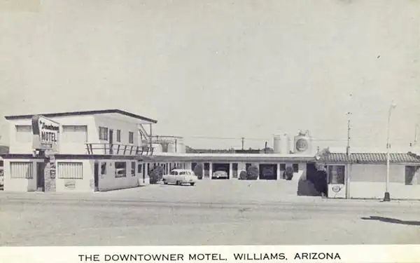 black and white 1950s postcard: U shaped motel, 2 story corner office, flat roof and neon sign