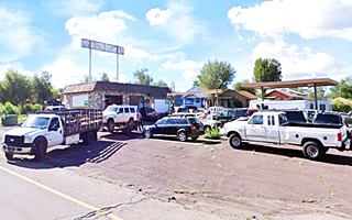 Fernow Texaco Ash Fork AZ old stone faced box shaped mansard roof station, whitewashed sign above it, detached canopy and many parked vehicles being repaired or towed