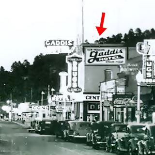 black and white photo at dusk, 1930s, cars, stores, building with neon sign and wall sign: GADDIS HOTEL