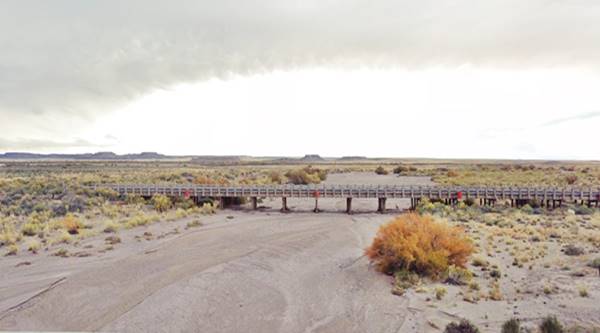 timber bridge across a wide dry river, bushes, gray clouds over the arid country