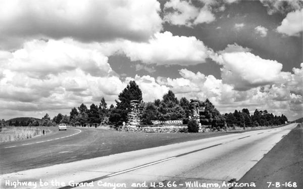 1950s black and white postcard: highway, junction, sign made of boulders, trees