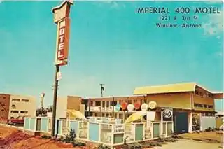1960s color postcard of a 2-story building with gullwing roof, a pool and neon sign