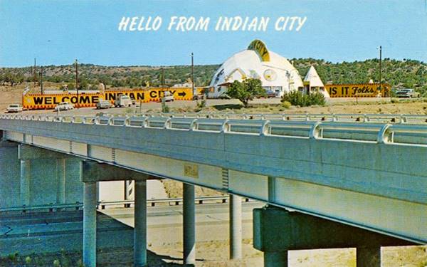 vintage postcard of a dome-shaped trading post with cars and a tepee seen from the other side of the Freeway overpass