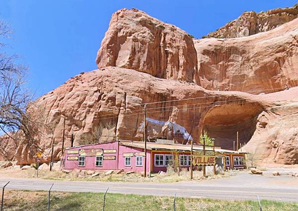 Indian Village Trading Post US66 Lupton faded red gable roofed, vacant building with broken windows and trading post signs, by imposing sandstone cliff
