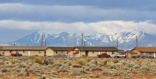 view of Leupp AZ: snow capped mountains in the distance, humble homes with pickups parked by them. Arid surroundings