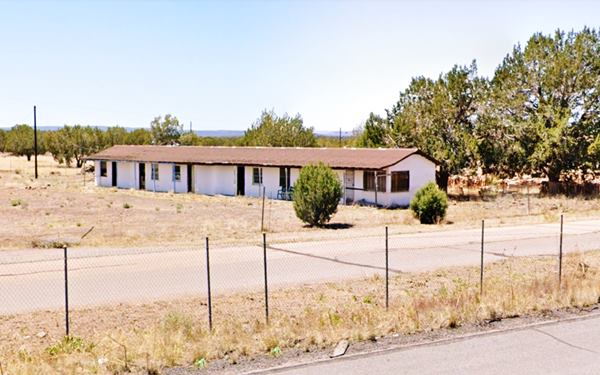 long, single floor gable roofed building, vacant, junipers in the yard, seen from the freeway