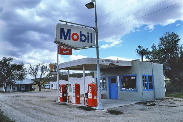 box shaped Mobil gas station, flat canopy, buildings beyond, trees, Mobil sign, and pumps