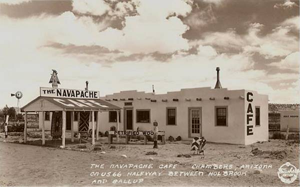 building with navajo style, canopy, rugs for sale and cafe sign, a black and white 1940s postcard