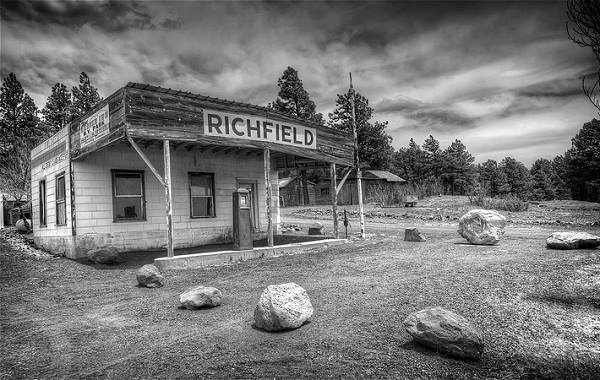 black and white photo of rickety woodframe building, with a gas pump, a Richfield sign and gravel driveway, pine trees behind