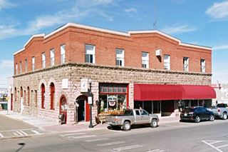 2-story corner building, rock faced 1st floor, red brick 2nd floor, cars, stores, people