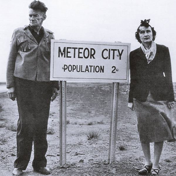 black and white photo c.1950s man and woman on each side of a sign that reads METEOR CITY POPULATION 2
