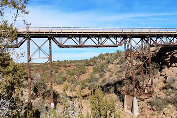 steel bridge with two steel piers crosses a steep narrow canyon with bushes on its walls