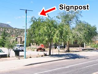 Singpost of old Qumacho Cafe green steel signpost stands by sidewalk, cars parked behind, US 66 in front