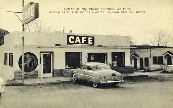 1950s black and white picture, white pueblo style Qumacho cafe with singpost to the left and motel with sign to the right