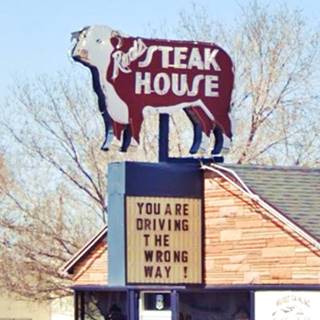 hereford on a neon sign, RODS STEAK HOUSE on it. Below it says words: YOU ARE DRIVING THE WRONG WAY!