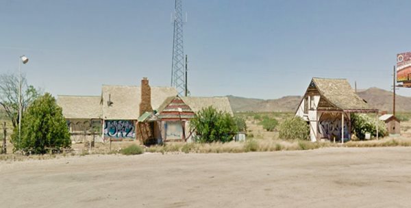 vacant ruins of buildings, trees and bluffs in the background: current view of Santa Claus Arizona inn and gas station