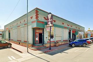 corner building, flat roof single story, bar on corner, neon sign, green tone painting. Parked cars