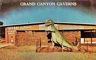 T-rex dinosaur statue at Grand Canyon Caverns 1960s 1960s postcard with T-rex statue by gable roof building, woman exiting it