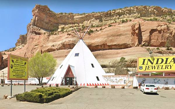 large white tepee with windows in it and yellow signs. Red cliffs behind