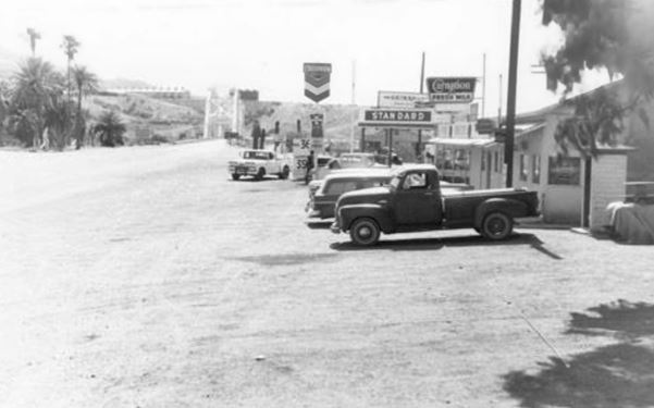 1960s black and white photo along US 66 with gas stations, trees, palm trees, mountains 
and the Colorado River bridge in the distance