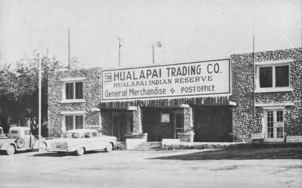 black and white 1950 photo, car, pickup, two story stone building with sign, alcove over entrance and vigas (logs) jutting out of wall