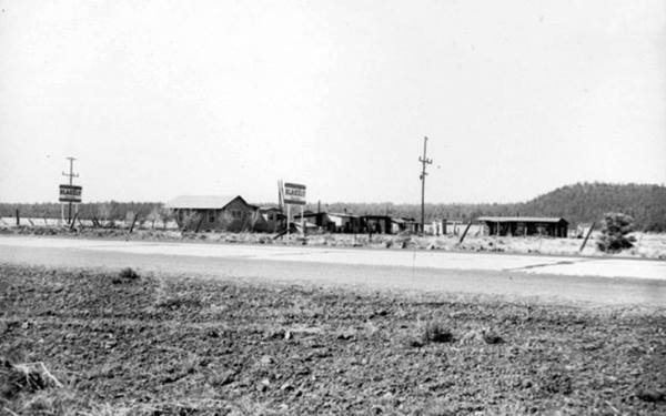 black and white photo of rickety buildings and trees, forested hills in the background, seen from Route66