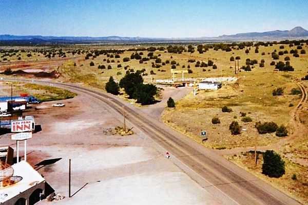 aerial photo looking SW, motel lower left, Sinclair station middle left, Route 66 cuts across from upper left to lower right and Whiting station next to some trees on the right side of the hihgway. Junipers on the dry landscape, hills in the distance
