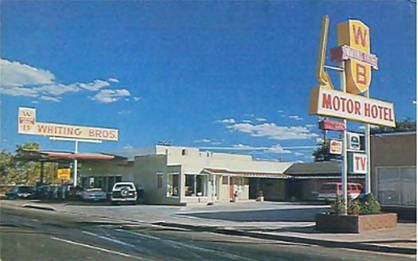 U-layout motel, flat roof, and a gas station with low gable roof canopy sign above canopy sayS WHITING BROS, motel sign says WB Motor Hotel.