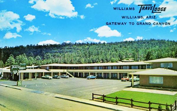 two story gable roof U-shaped layout of a motel 1960s postcard, pine trees on hill behind