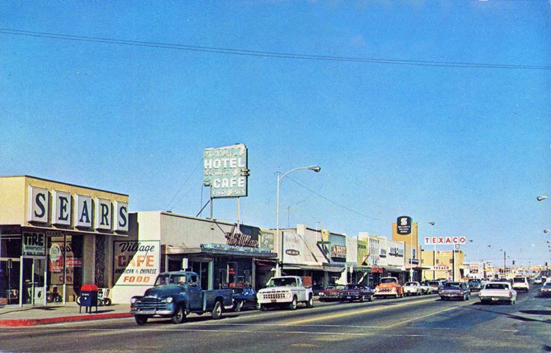 North side 200 block of Main St. Barstow CA, 1960s street (US66), stores, cars, neon signs, sunny day 1960s color view