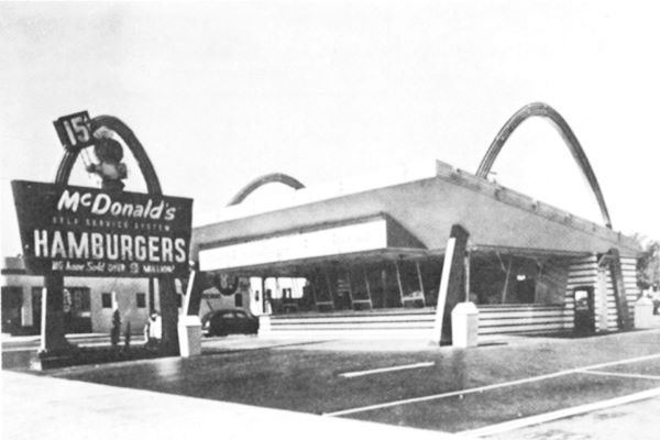 black and white, 1953 McDonalds with arches on each side of a building, car, and neon sign