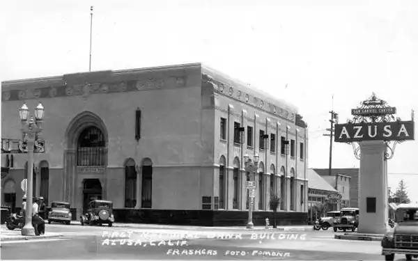 By Bob Frasher, Foothill Blvd. and Azusa Ave. 1939s, 1st Nat. Bank of Azusa black and white 1939 view of the 1st Nat Bank 2 story block shaped building on a corner, a sign reading AZUSA on top of a column to the right, traffic, cars