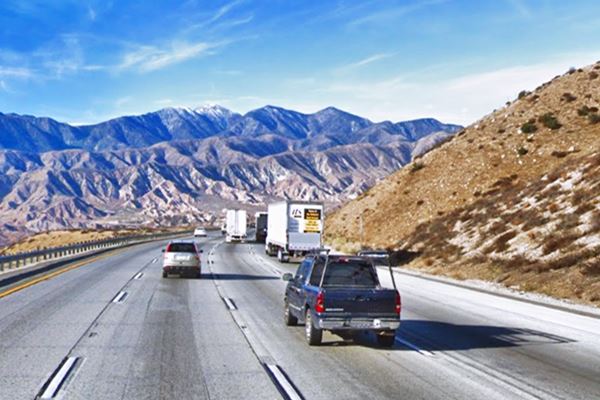 I-15 in Cajon Pass, 2020s color, freeway in arid shrub covered hills, snowcapped mountains in the distance