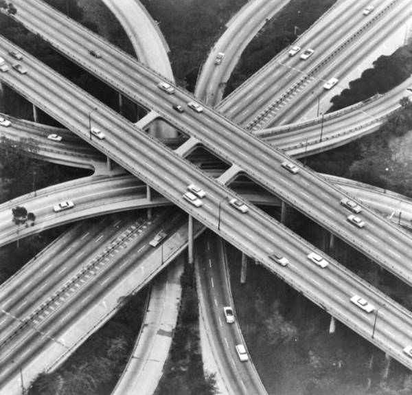 4-level internchange c.1960 Los Angeles CA Route 66 black and white photo, aerial view of two freeways crossing at right angles, each with 4 lanes in divided highways and curving lanes linking them, cars drive on the lanes c.1960