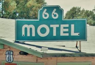 zoom into a neon sign that reads in white and green: 66 MOTEL, on a shingle rooftop