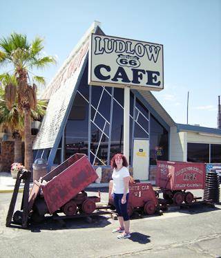 Perla Eichenblat at Ludlow Cafe woman standing by mining carts in front of steep roofed Ludlow Cafe
