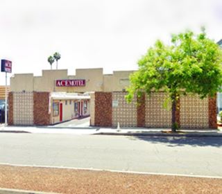 motel facing Route 66, trees. units along a central drive, walled parapet. Sign on the left