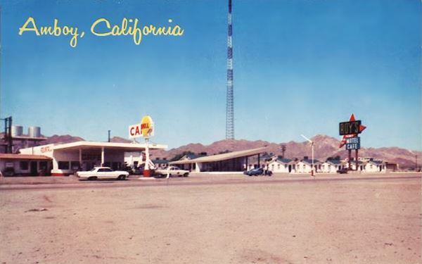 Amboy 1960 postcard US 66 left to right, gas station,Shell, cafe with slanting roof, motel units (cabins) and neon sign, cars and US 66 in front, hills and radio antena behind 1960 color postcard