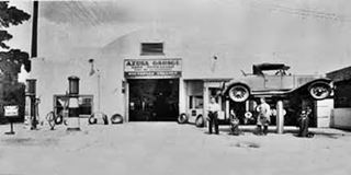 1932 Azusa Garage on Rte 66 Azusa CA black and white 1932, two men by garage sign reads AZUSA GARAGE, facing US66, car in the air on a jack to the right, 2 gas pumps left